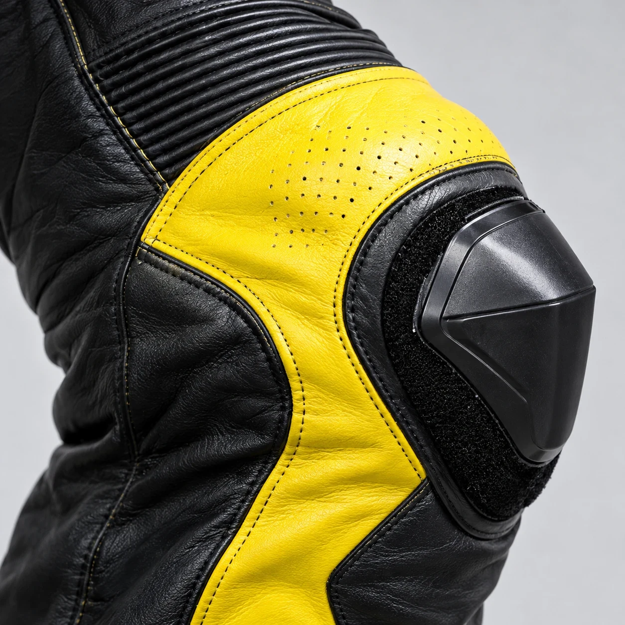Close-up of the knee: hard knee slider on a hook-and-loop base, perforated coloured leather and accordion stretch above the knee